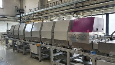 Figure 1: In-line coating machine at the AELab in Karlstein, Germany showing eight compartments. The sample carrier is inserted in the far left. Silicon oxide is dynamically deposited in the right compartment (purple hood) by moving the sample carrier beneath the rotatable magnetrons.